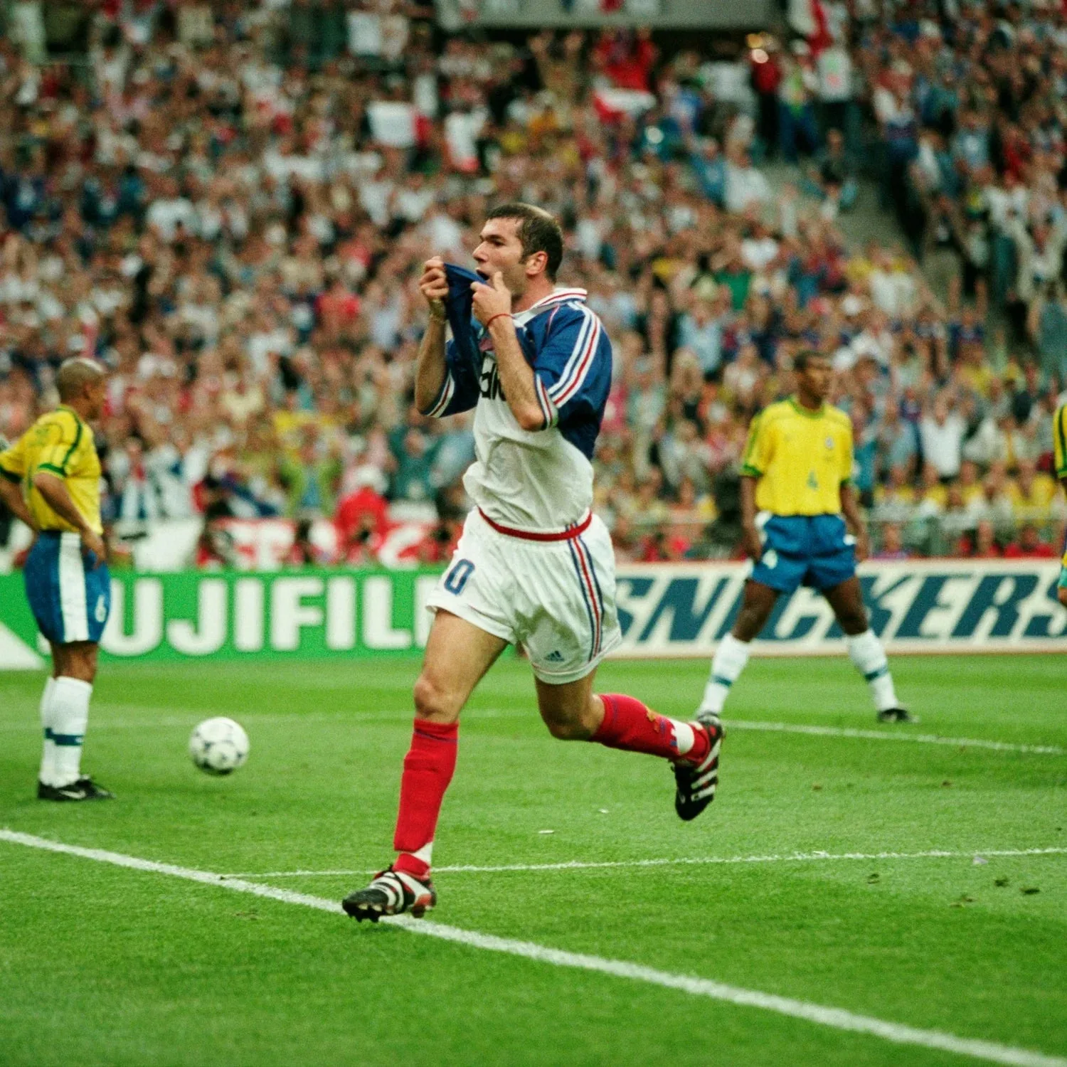 Joueur en maillot rétro bleu et blanc fêtant un but devant des tribunes pleines